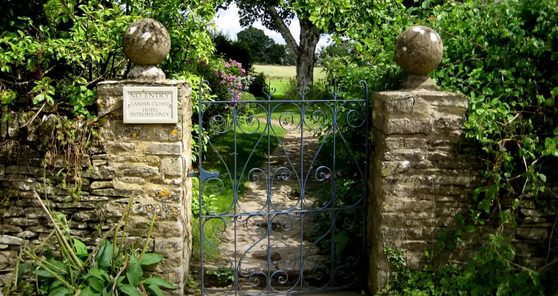 Garden Entrances and Stone Work Elegant garden entrance with ornate iron gate and stone pillars surrounded by lush greenery
